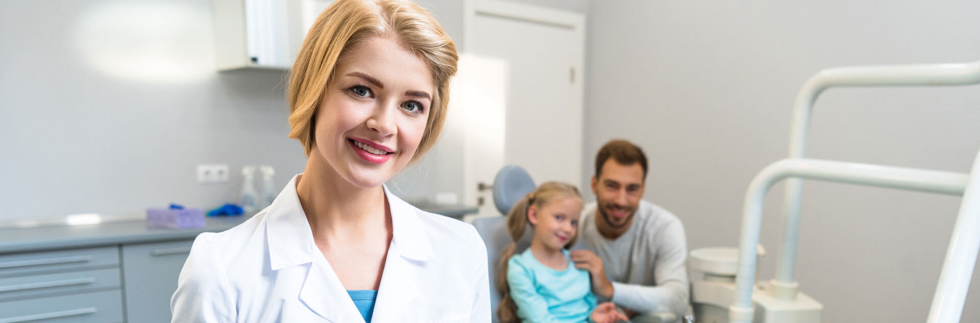 Dental assistant smiling at the camera with small kid and male person behind